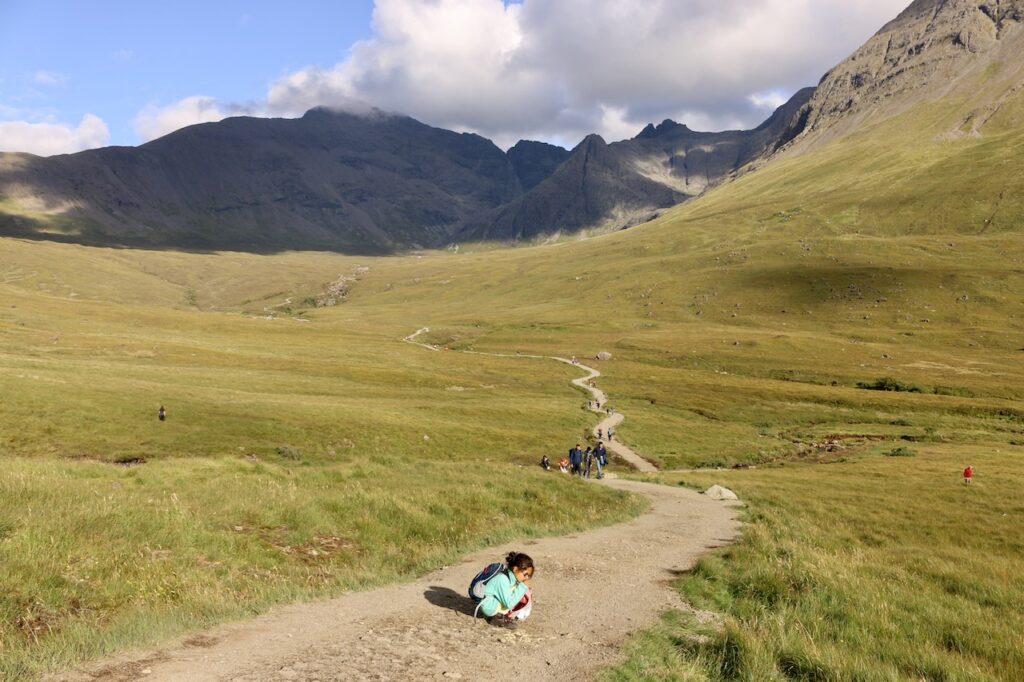 A child sitting on a rural path in the Scottish Highlands.